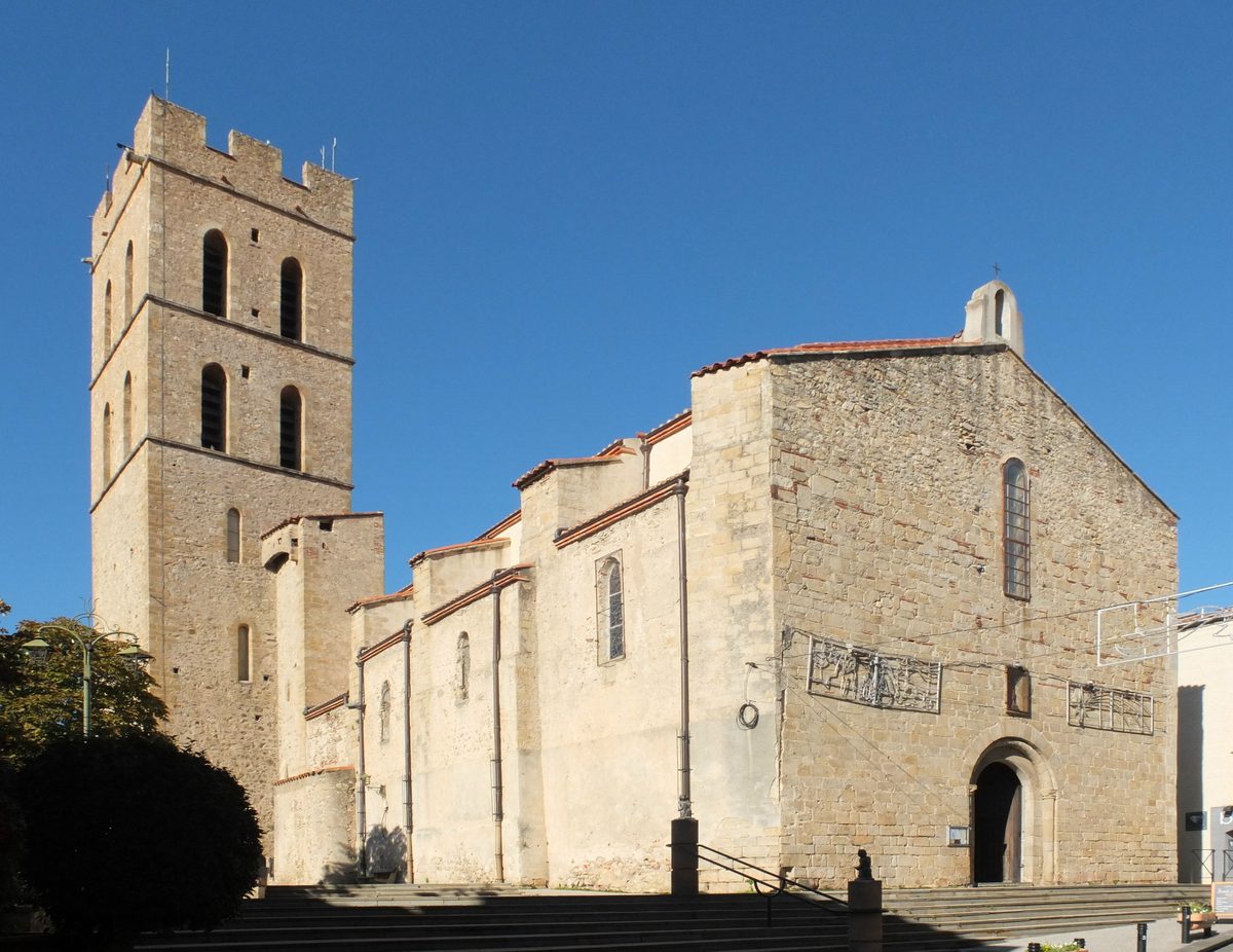 The Notre-Dame-del-Prat church in Argelès-sur-Mer, its crenellated bell tower and stone façade under a blue sky