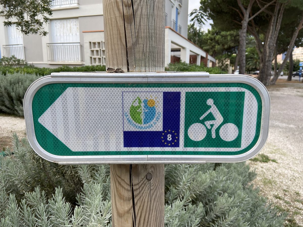 Sign for the « La Méditerranée à vélo » cycle route (EuroVelo 8) in Argelès-sur-Mer, under the pine trees
