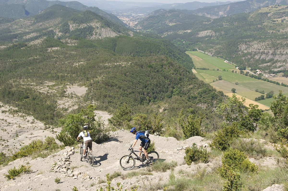 Two mountain bikers on a stony mountain trail above a valley